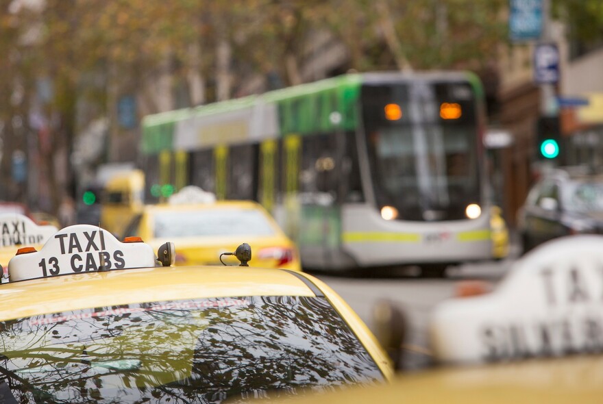 Row of yellow taxis on a street and a tram in the background. 