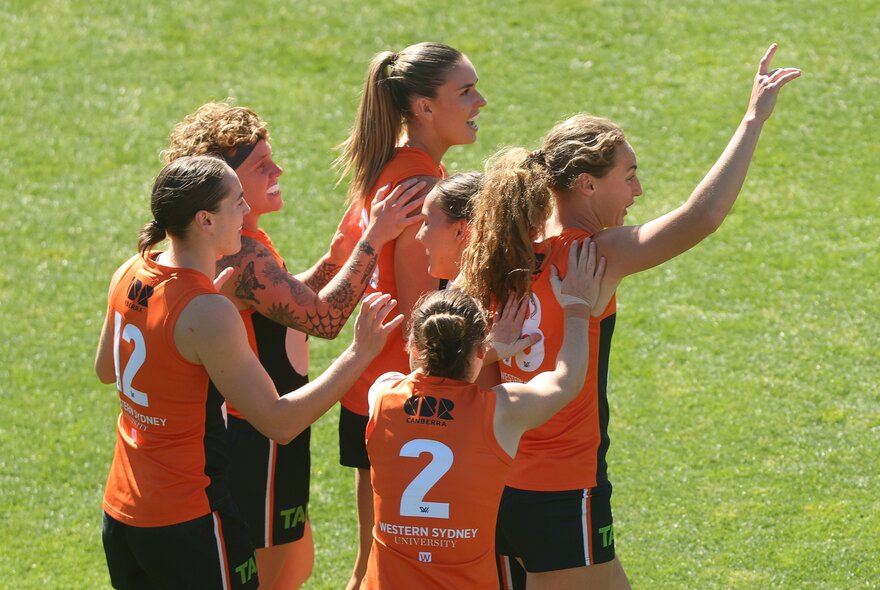 GWS Giants AFLW players celebrating on the field, coming together in a group huddle.