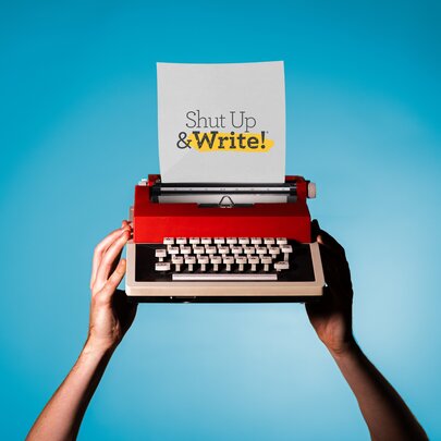 Hands holding up a red typewriter with a sheet of paper reading 'shut up and write'.