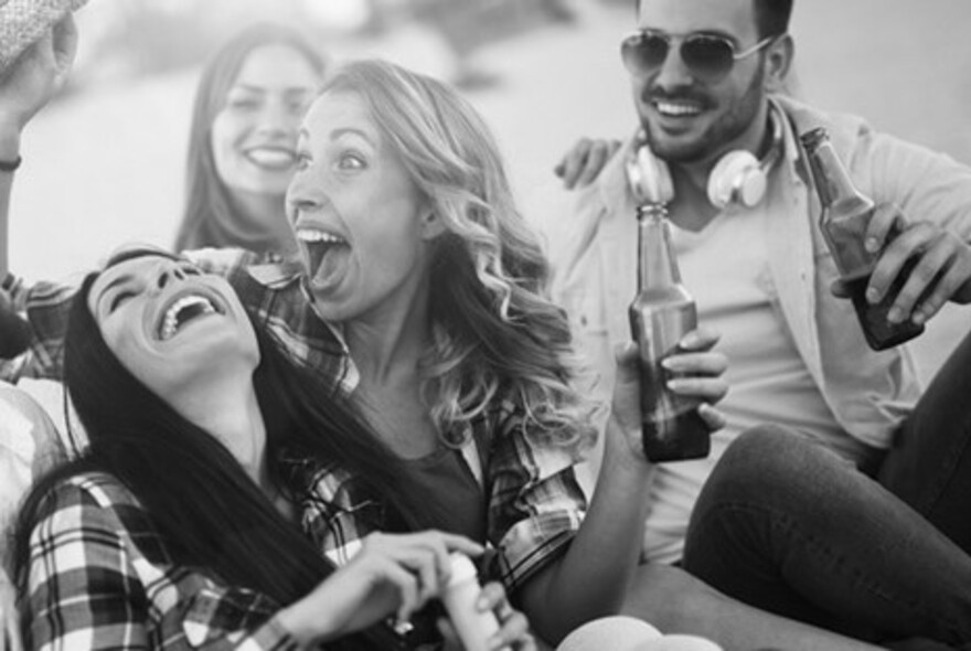 A black and white image of people laughing and holding bottles of beer. 