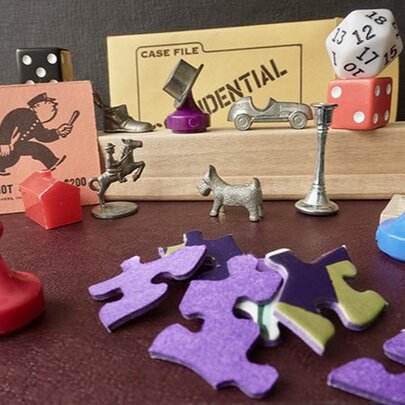 A collection of board game pieces, including puzzle pieces, Monopoly markers and cards, dice and coloured game markers.