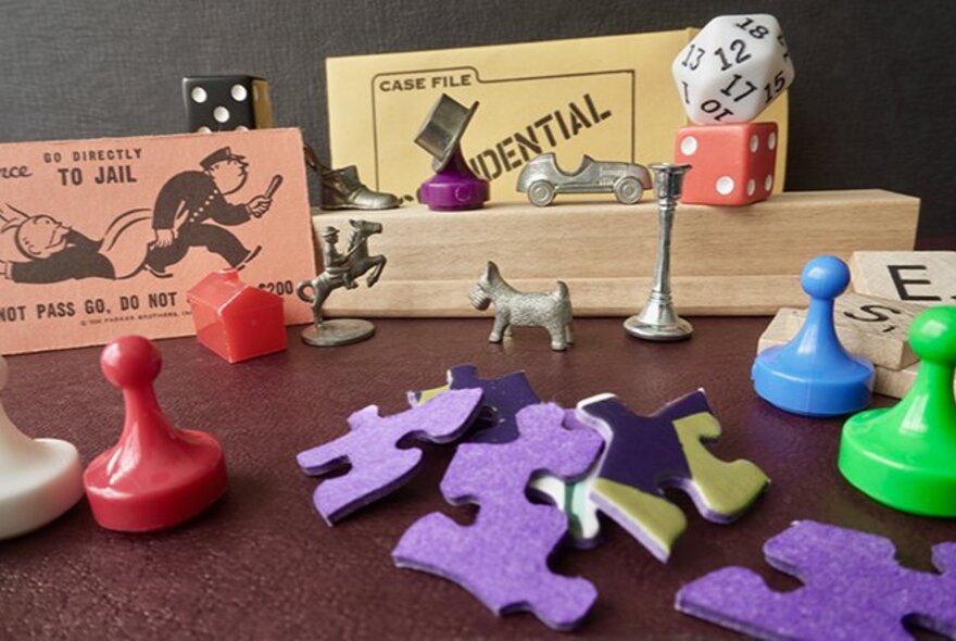 A collection of board game pieces, including puzzle pieces, Monopoly markers and cards, dice and coloured game markers.