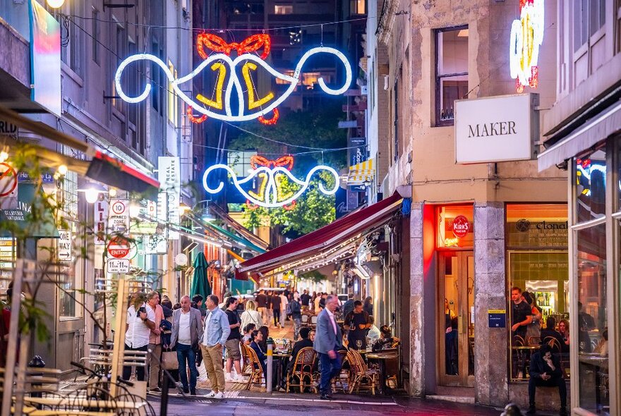 People dining in a busy laneway under Christmas decorations.