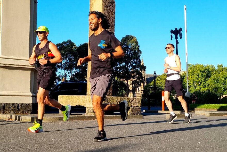 Three people running past a building in Carlton Gardens on a bright day.