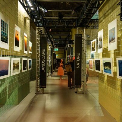 An exhibition space featuring photography zones like Landscape and Nature with photos hanging on room dividers; part of the SceneScape expo.