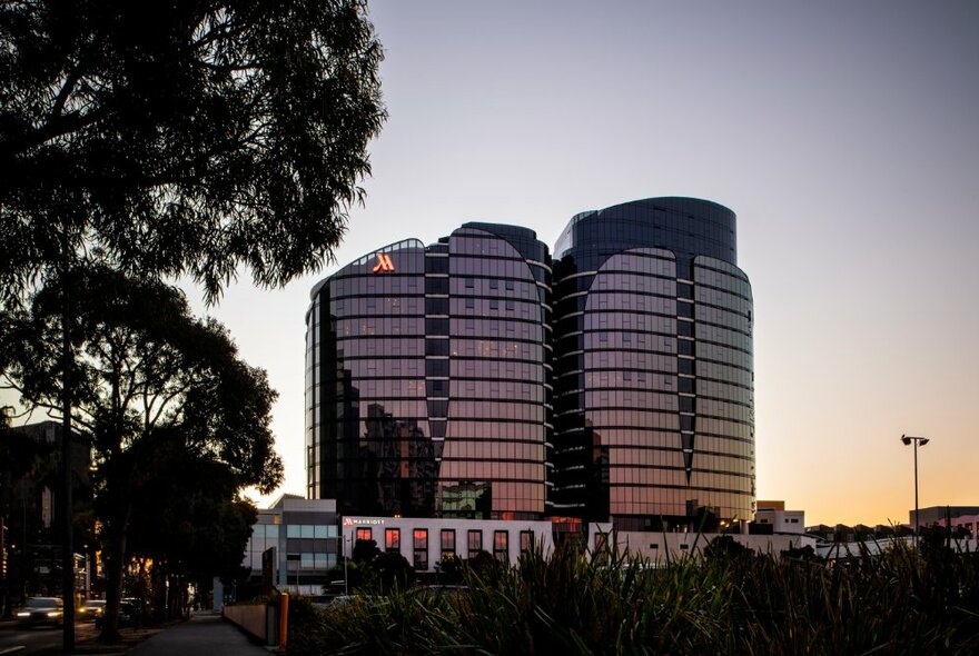 Sunset view of the Melbourne Marriott Hotel with large gum trees in the foreground.