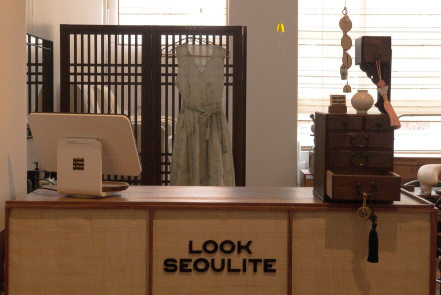 The wooden payment counter at a clothing shop, with a small set of antique drawers on the top and a dress hanging behind.