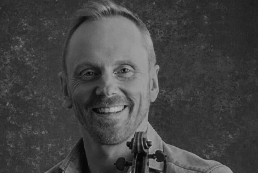 Man with short blond hair and stubble holding a violin.