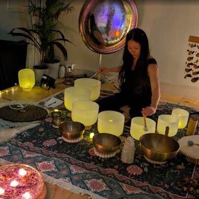 A person conducting a meditation exercise with cosmic gongs and vessels for sound resonance arranged on a Persian rug.