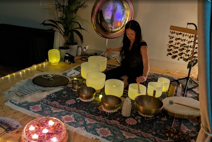 A person conducting a meditation exercise with cosmic gongs and vessels for sound resonance arranged on a Persian rug.