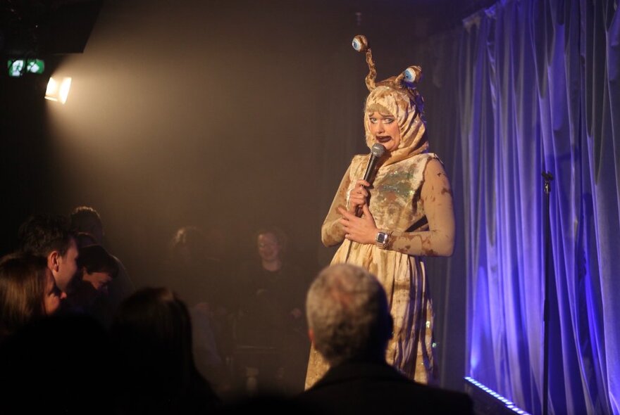 A comedian on a small stage performing wearing an insect costume. 