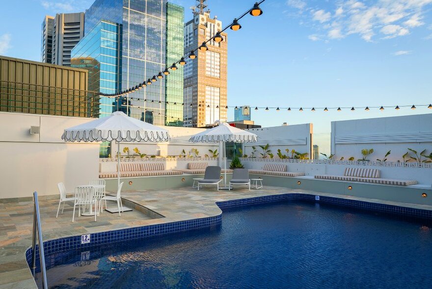 A rooftop pool with umbrellas and string lights.