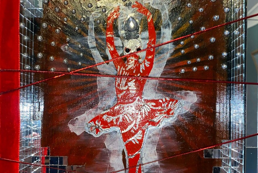 An artwork featuring a central figure in a red ballet costume with white patterns, set against a brown and gold background with white, ghostly figures and red strings stretched across the composition.