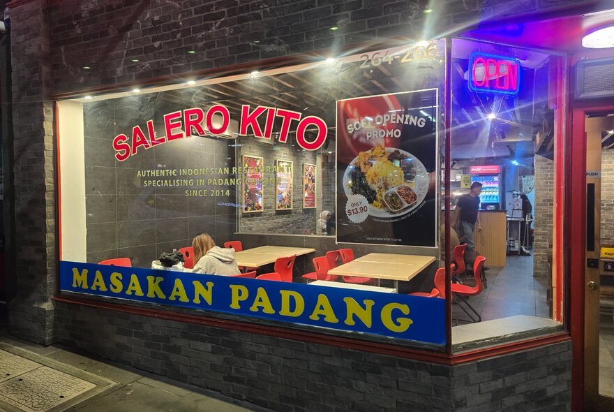 Shopfront at night with signage and lights.