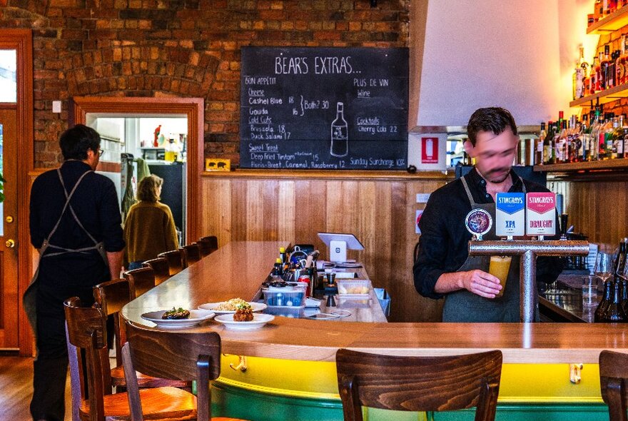 Inside a wine bar there is a bar tender pouring a beer. 