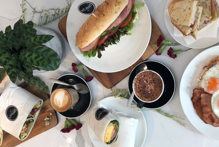 A table with an array of dishes including coffees, wraps and rolls.