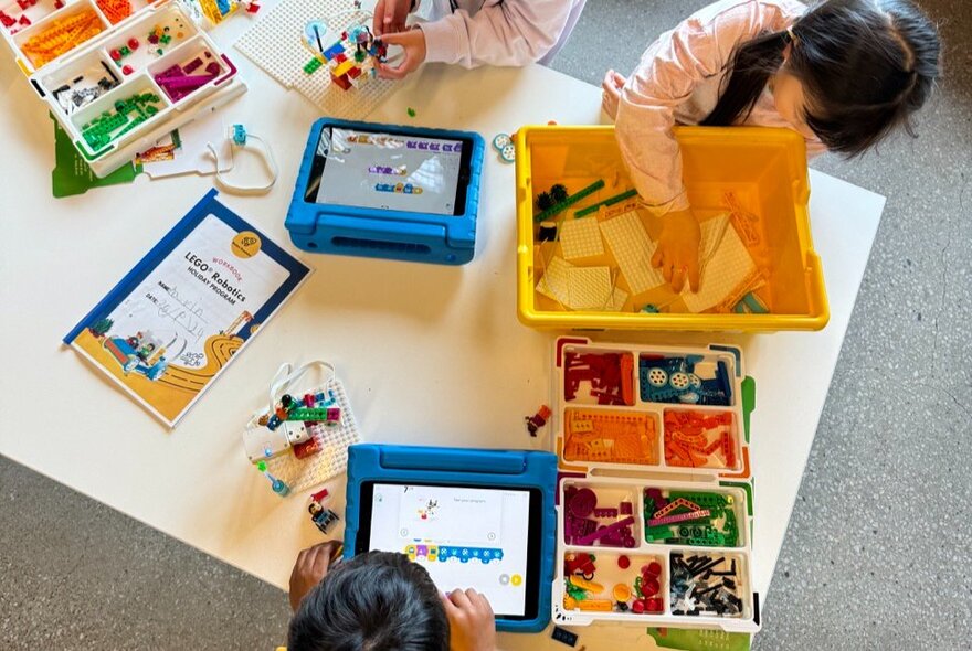 Kids engaging in a LEGO robotics workshop, using digital devices and LEGO bricks to build robotic models.