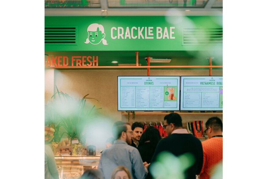 People lined up at the counter of the banh mi cafe Crackle Bae waiting to order, the rear wall displaying a menu and signage for the shop.