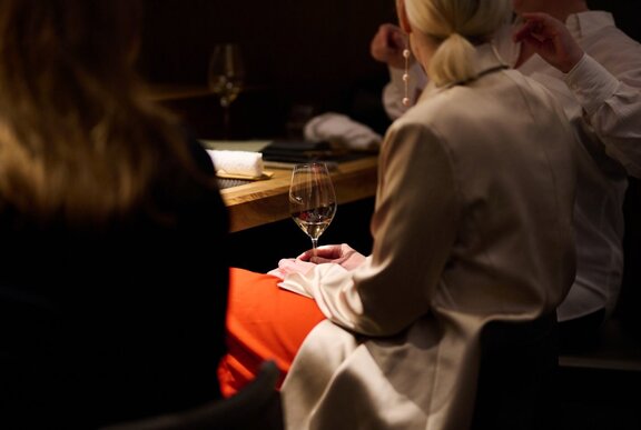 Woman seated at a restaurant table holding a glass of wine on her serviette and lap.
