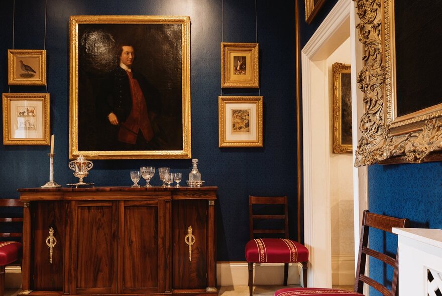 Period room with dark blue gloss painted walls, framed pictures and wooden furniture.