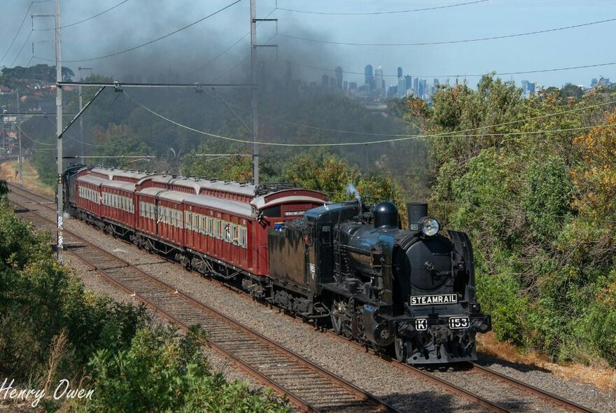 Steam train making a head of black steam on a track surrounded by trees.