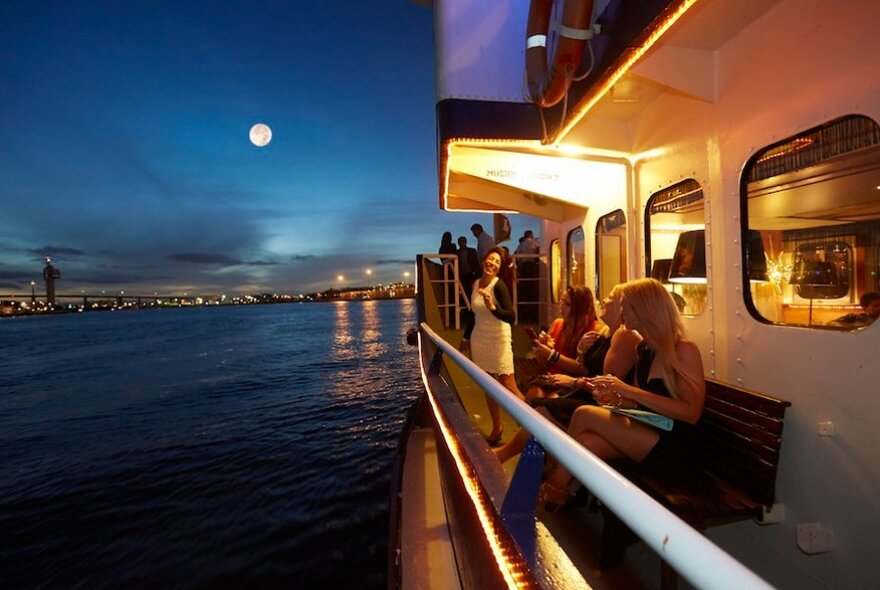 People along the side deck of a boat, with full moon in the background.