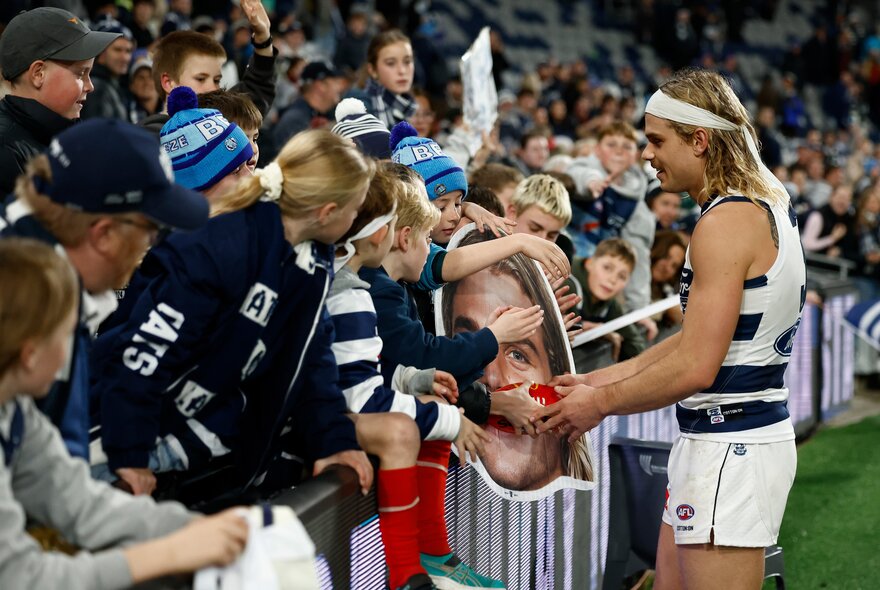 Geelong AFL player greeting fans in the stands during a match.