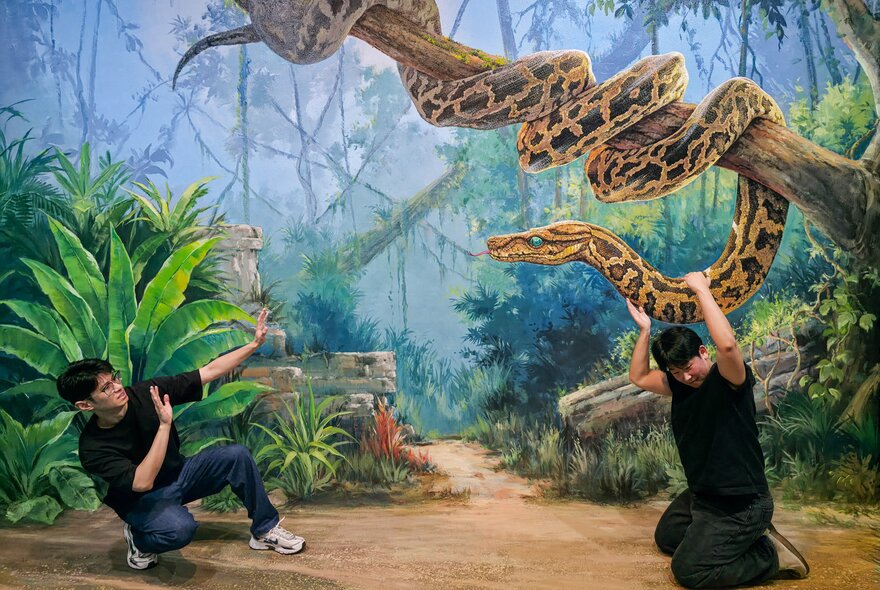 Two friends in exaggerated poses against a hand-painted interactive artwork of a jungle scene, at ArtVo.