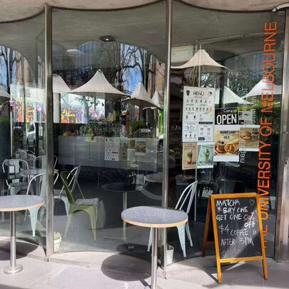 A university cafe with tables outside the curved glass windows with a menu board at the entrance.