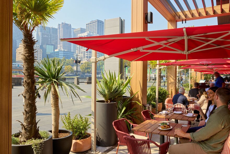 Two friends are drinking cocktails at an outdoor restaurant under a red sun umbrella. 