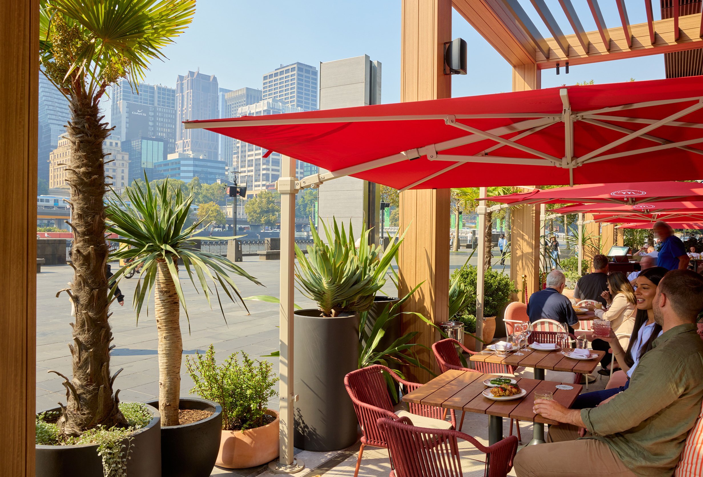 Two friends are drinking cocktails at an outdoor restaurant under a red sun umbrella. 