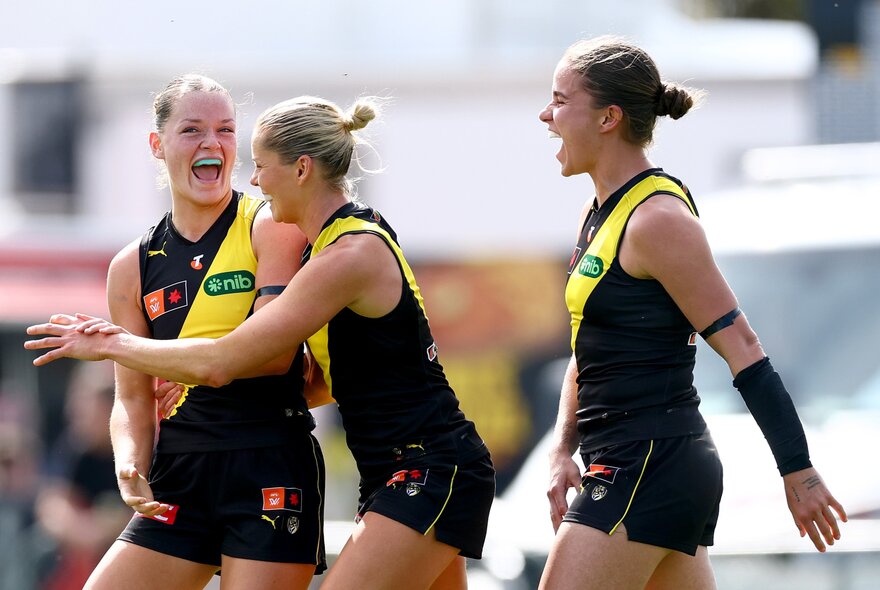 Richmond AFLW players celebrating on the field in their yellow and black guernseys.