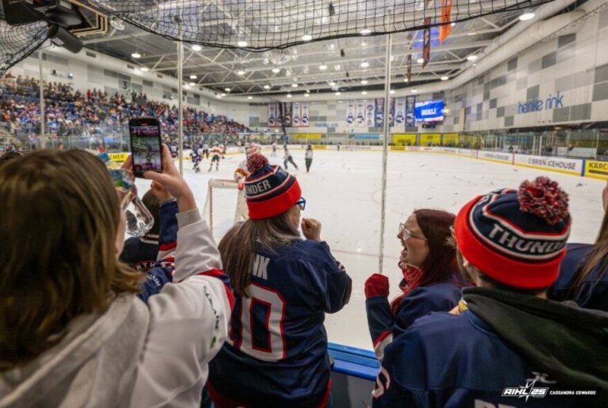 Fans seated behind the ice rink watching a game.