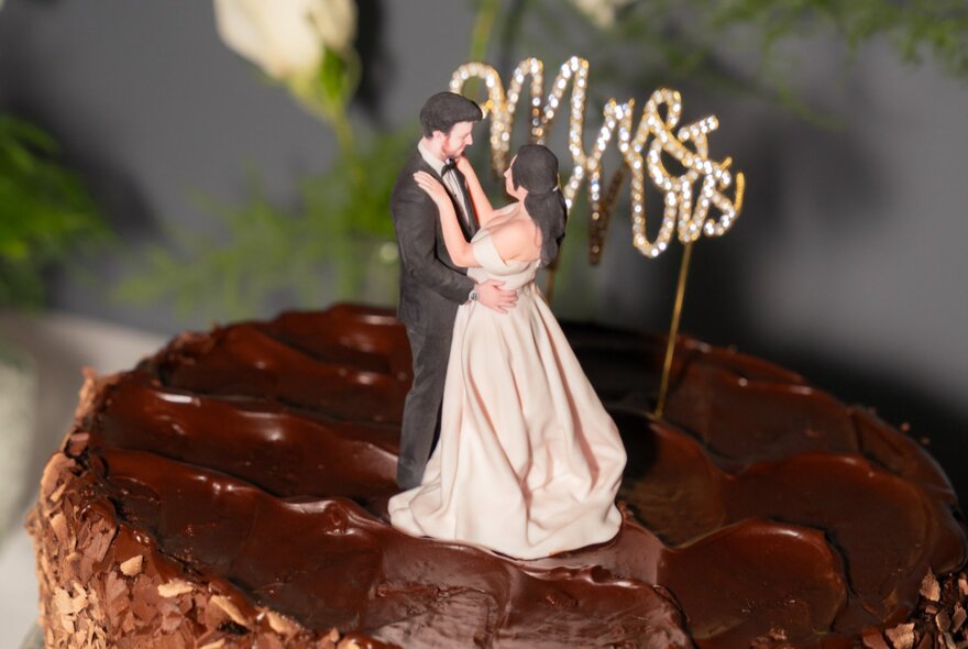 A 3D printed figurine of a wedding couple on top of a chocolate cake along with a 'Mr & Mrs' sign.