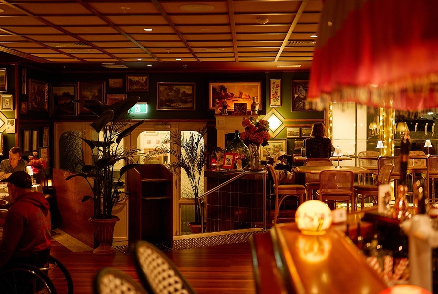 The moody interior of a restaurant with framed photographs and paintings on the wall.