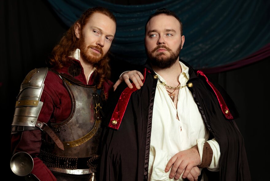 Two men dressed in medieval costumes one with his hand on the other's shoulder.