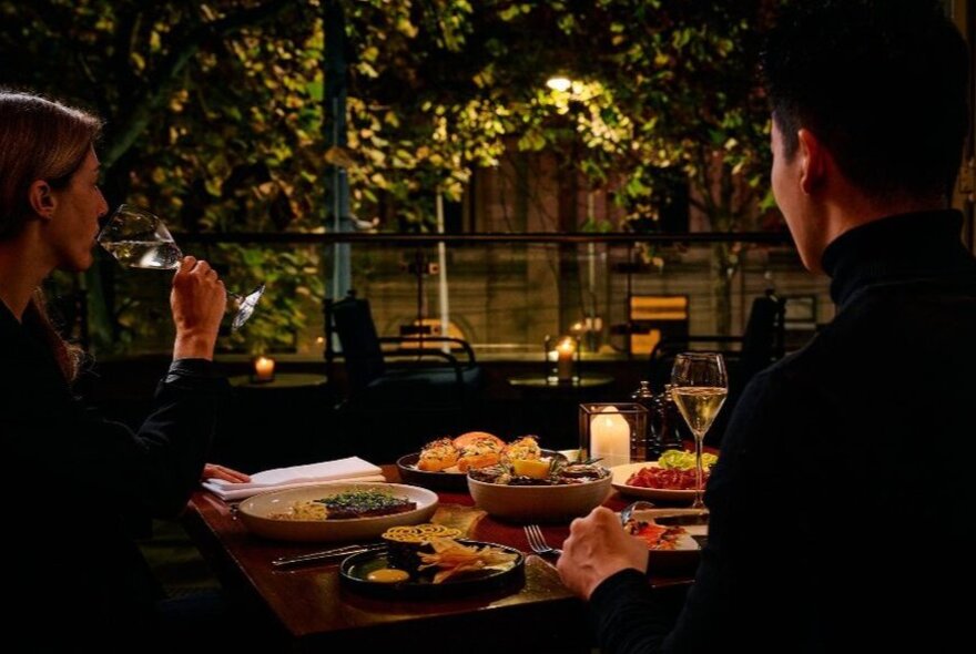 A couple dining among trees in a dark restaurant.