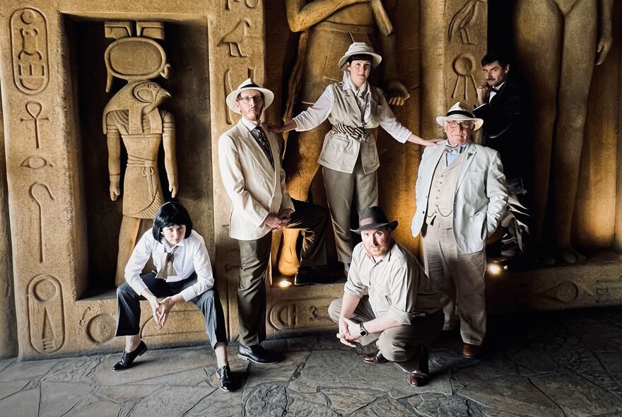 Five people dressed in 1920s explorer costumes standing in front of a wall of Egyptian hieryoglyphics.