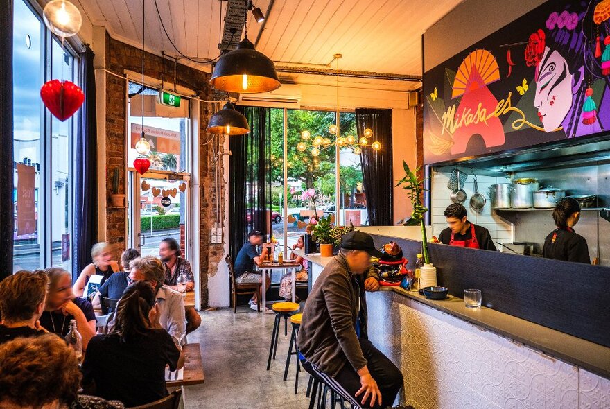 People are eating inside a Latin Asian restaurant. There is a colourful mural of a woman on the wall.