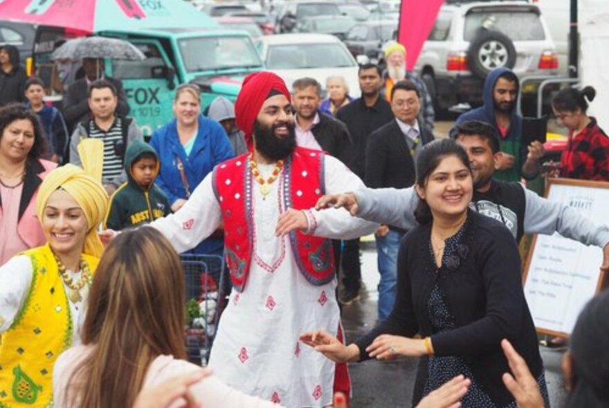 Indian dancers in traditional dress dancing in a circle in a car park.