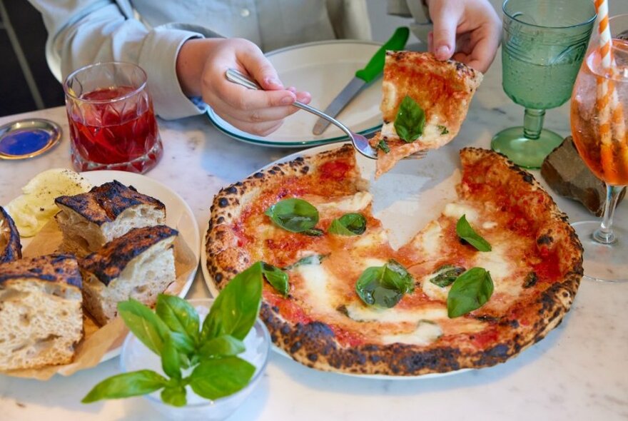 A close up of someone serving themselves a slice of margherita pizza.