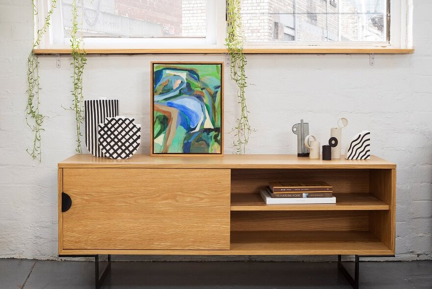 A wooden side board topped with a framed artwork and black and white ceramics.