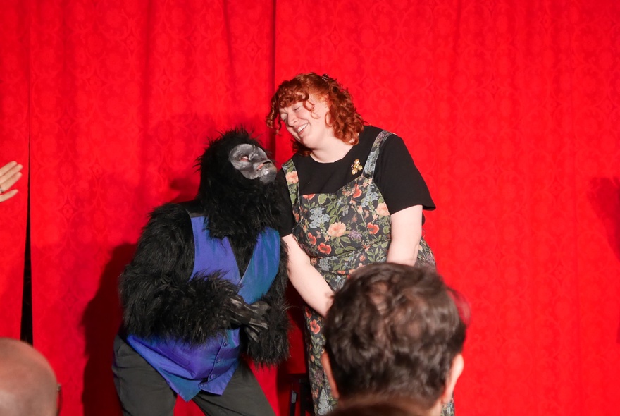 Two improv actors on stage, one in a gorilla suit wearing a waistcoat, performing in front of an audience.