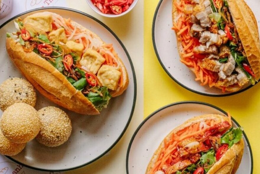 Three banh mi on plates with different fillings.