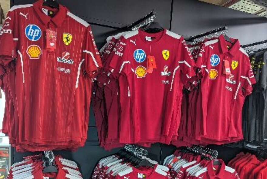 Racks of red F1 Ferrari branded polo shirts on display in a shop.