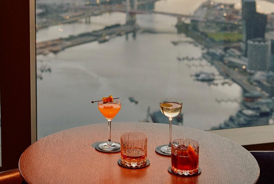 A table with four different cocktails with a view out over the city and river.