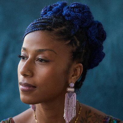 Poet aja monet lookign to her right with a serene expression and long tasseled earrings.