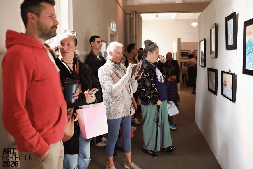 People in a corridor viewing artwork the walls. 