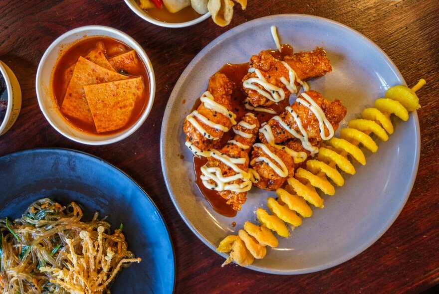 Korean street food dishes including spicy tofu, chicken and potato swirl on a stick.