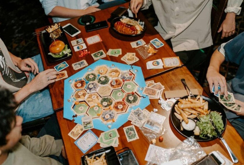 A group of friends playing Settlers of Catan with plates of pub food.